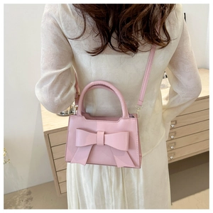 Detail of a pink handbag featuring a large decorative bow and a round top handle