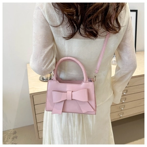 Woman carrying a pink PU leather handbag with a large bow detail and thin shoulder strap
