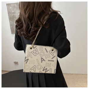 Detailed close-up of beige shoulder bag with golden chain and letter print texture
