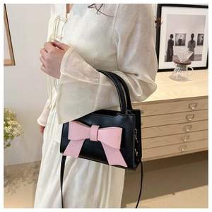 Detail view of a black mini square handbag featuring a large pink leather bow and shoulder strap