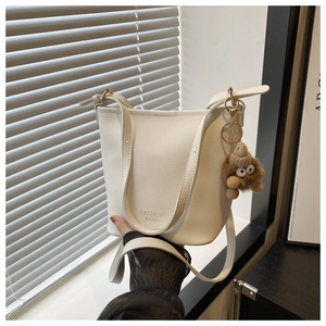 Gros plan du sac seau blanc texture litchi avec lettrage embossé et pendentif en peluche