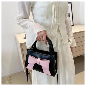 Detail of a vintage black leather handbag with a large pink bow and round handle