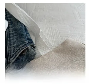 Close-up of beige canvas bag texture with white strap and blue denim jacket metal button