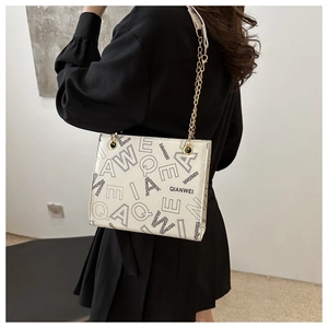 Detailed side view of beige shoulder bag with black lettering and gold chain strap