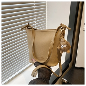 Détail du sac seau beige texturé avec pendentif monstre en peluche et bandoulière