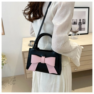 Detail of vintage black leather bag featuring a large pink bow and slender strap