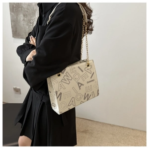 Close-up of beige letter print shoulder bag with gold chain strap worn by a model
