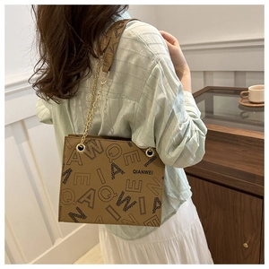 Detail of a brown shoulder bag with letter prints and gold chain strap shown on a model
