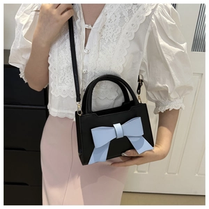 Detail of black crossbody bag with light blue bow and gold hardware on white lace shirt