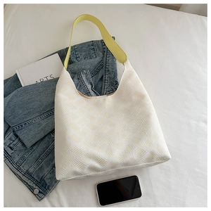 White quilted hobo bag with yellow strap shown styled with jeans and book on bed