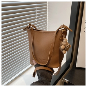 Détail du sac seau en cuir marron à motif litchi avec charm d'ours et logo de mode