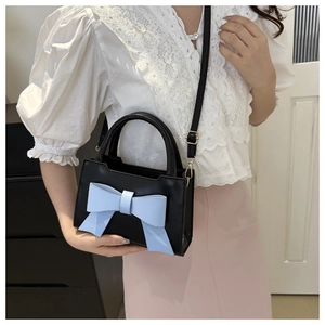 Detail of black crossbody bag featuring a large light blue leather bow and gold hardware