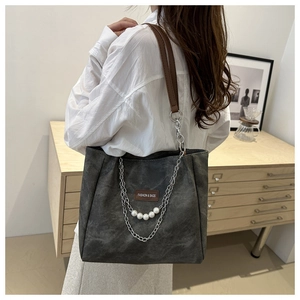 Dettaglio della borsa tote grigia con catena argento, ciondoli di perle e etichetta moda