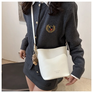 Détail d'un sac seau blanc à texture grainée avec un pendentif ours marron