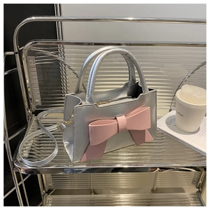 Detail of silver metallic tote bag featuring a large pink bow on a display shelf