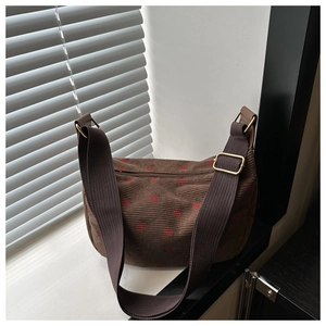 Détail du sac demi-lune en velours côtelé marron avec broderie fraise et large bandoulière