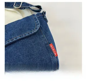 Detailed close-up of dark blue denim shoulder bag with orange stitching and silver buckle
