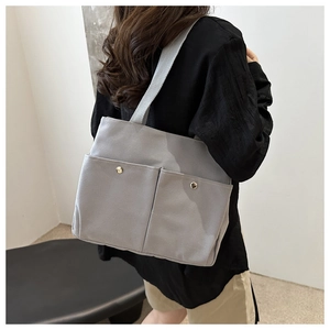 Detail of grey canvas tote bag featuring double front pockets and metal button closures