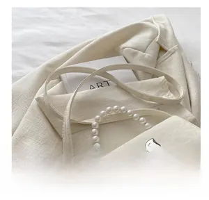Detailansicht der cremeweißen Umhängetasche mit Perlenhenkel und Silberschleife auf Blazer