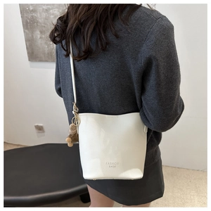 Détail d'un sac seau crème avec texture litchi et pendentif ours en peluche