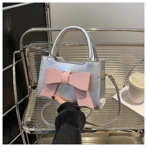 Detail of silver metallic handbag featuring a large pink bow and sleek round handle