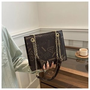 Detailed view of dark brown leather tote bag with gold chain strap and letter print
