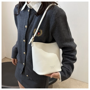 Gros plan d'un sac seau blanc avec texture galet et bandoulière sur un cardigan gris