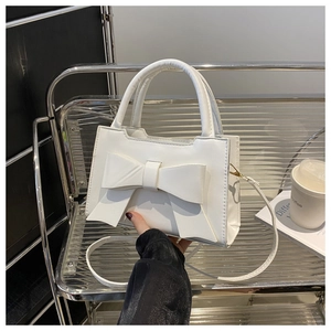 Detail of white bow handbag showing matte leather texture and elegant carry handle