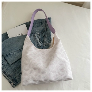 Detail of white textured fabric tote with a wide lavender strap placed on blue denim