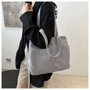 Detail view of a large grey canvas tote bag with functional pockets worn by a model