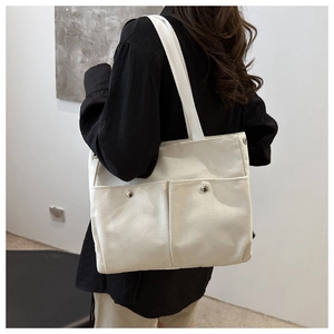 Detail view of beige canvas tote bag with front magnetic pockets and wide shoulder strap