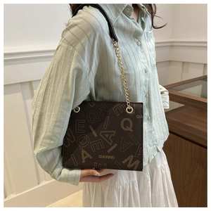 Close-up of texture leather shoulder bag with gold chain strap and letter prints