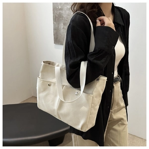 Detail of canvas tote bag showing front pockets and metallic snaps on cream fabric