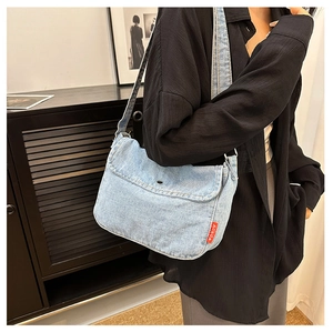 Detail of light blue denim crossbody bag with black buckle and red side brand label