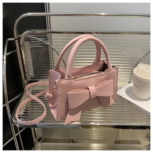 Pink PU leather handbag with oversized bow detail and gold zipper on a metal shelf