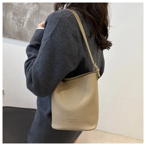 Sac seau beige en cuir litchi porté par un mannequin pour un style décontracté