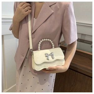 Detail of elegant cream handbag featuring a pearl handle and silver bow on wavy flap