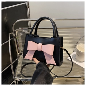 Detail of black faux leather handbag featuring a large pink bow decoration and smooth finish