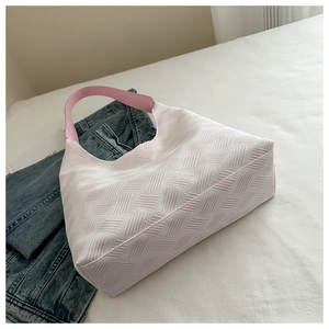 Detail of white tote bag featuring woven texture and soft pink shoulder strap on bed