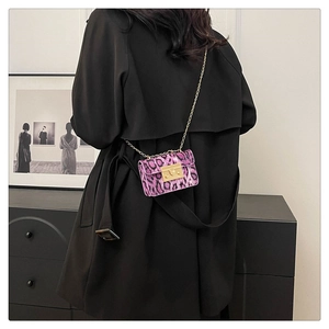 Dettaglio di mini borsa leopardata viola con catena dorata su cappotto nero