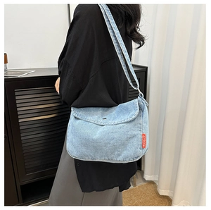 Detail of light blue denim tote bag with red woven side label in casual urban setting