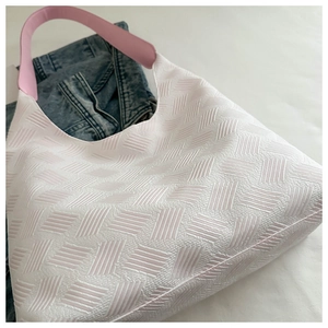 Close-up of white textured bubble fabric tote with pink leather handle on denim jeans