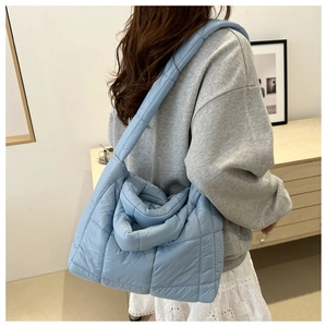 Close-up of a light blue quilted tote bag with wide shoulder straps worn by a model