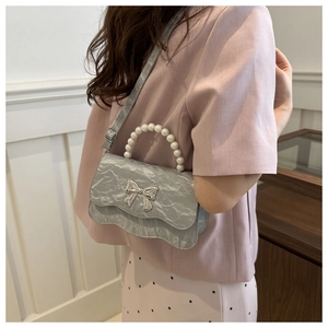 Detailed view of silver metallic pleated handbag with pearl handle and bow decoration