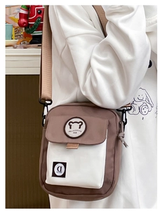 Detail of cute bear emblem and adjustable wide shoulder strap on brown canvas bag