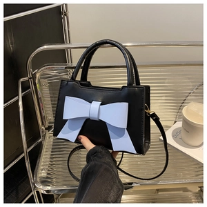 Close-up of black handbag with a bold light blue 3D bow on a minimalist shelf