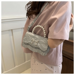 Detail of silver crinkled texture bag with pearl handle and metal bow on model