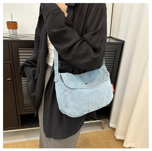 Detail of light blue denim crossbody bag with adjustable strap and red side label