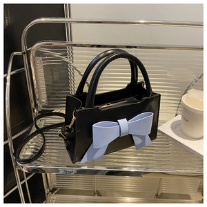 Detail of black faux leather handbag featuring a large light blue bow and gold zipper