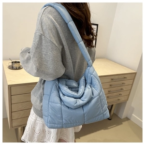 Back view of a model wearing a light blue quilted tote bag with soft puffer padding texture
